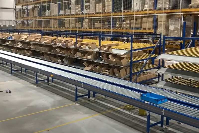 Sistema transportador de almacén con rodillos accionados por eje lineal