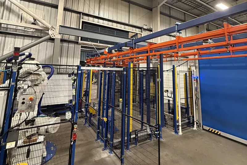 Transportador MCM Autotrack integrado con equipos de producción automotriz. Amber Industries overhead conveyor installation positioned above automated automotive manufacturing equipment
