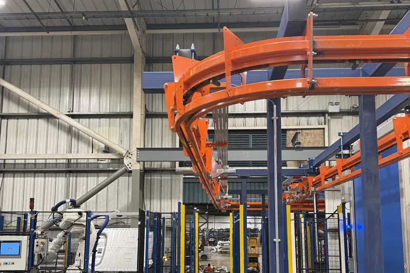 Sistema de transporte motorizado y libre con equipos de fabricación robótica. MCM Autotrack Power and Free conveyor system installed above robotic manufacturing equipment and safety guarding