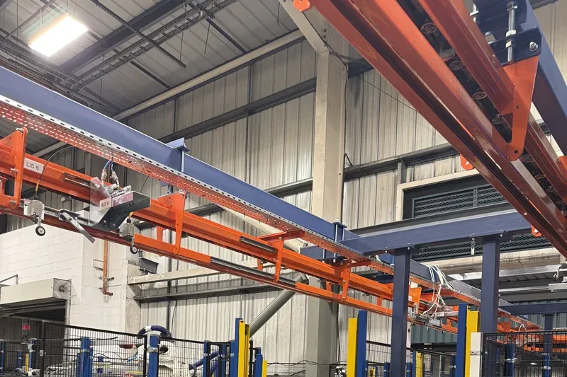 Sección de transportador aéreo curvo MCM Autotrack Close-up of curved orange MCM Autotrack overhead conveyor track within an automotive manufacturing facility